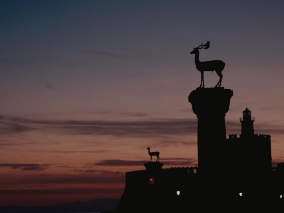 A picture showing sunset colours (pink, purple, peach) and the statue of the Dama-Dama deer of Rhodes